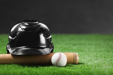 Photo of Baseball bat, batting helmet and leather ball on green grass against dark background, closeup. Space for text