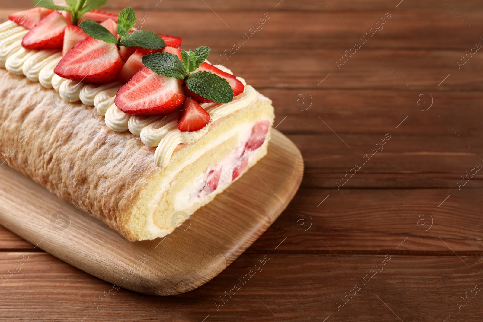 Photo of Delicious cake roll with strawberries and cream on wooden table. Space for text