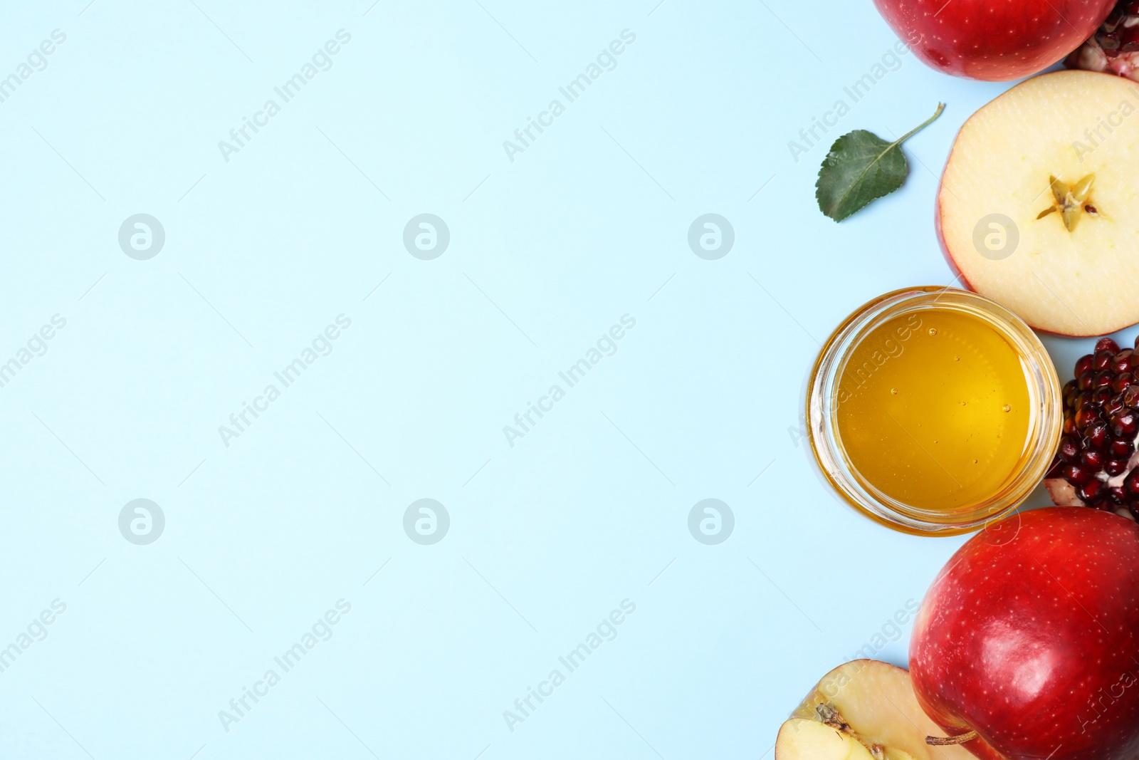 Photo of Honey, apples and pomegranate on light blue background, flat lay with space for text. Rosh Hashanah holiday