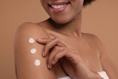 Photo of Young woman applying body cream onto arm on beige background, closeup
