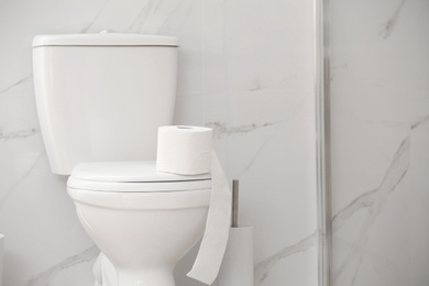 Photo of Modern toilet bowl with roll of paper in bathroom