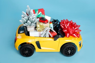 Child's electric car with toys, gift boxes and Christmas decor on light blue background