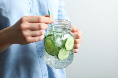 Photo of Young woman holding jar with fresh cucumber water, closeup. Space for text