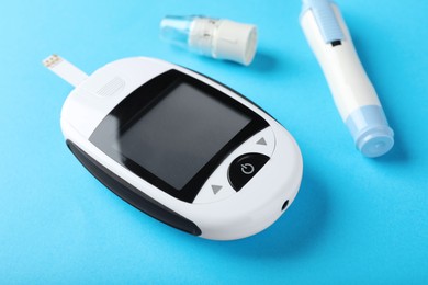 Digital glucometer and lancet pen on light blue background. Diabetes control
