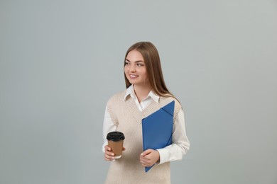 Teenage student with folder and paper cup of coffee on grey background