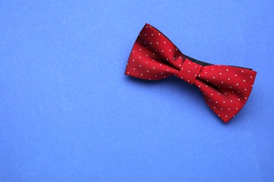 Photo of Stylish burgundy bow tie with polka dot pattern on blue background, top view. Space for text