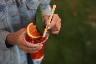 Young woman with plastic cup of refreshing drink outdoors, closeup. Space for text