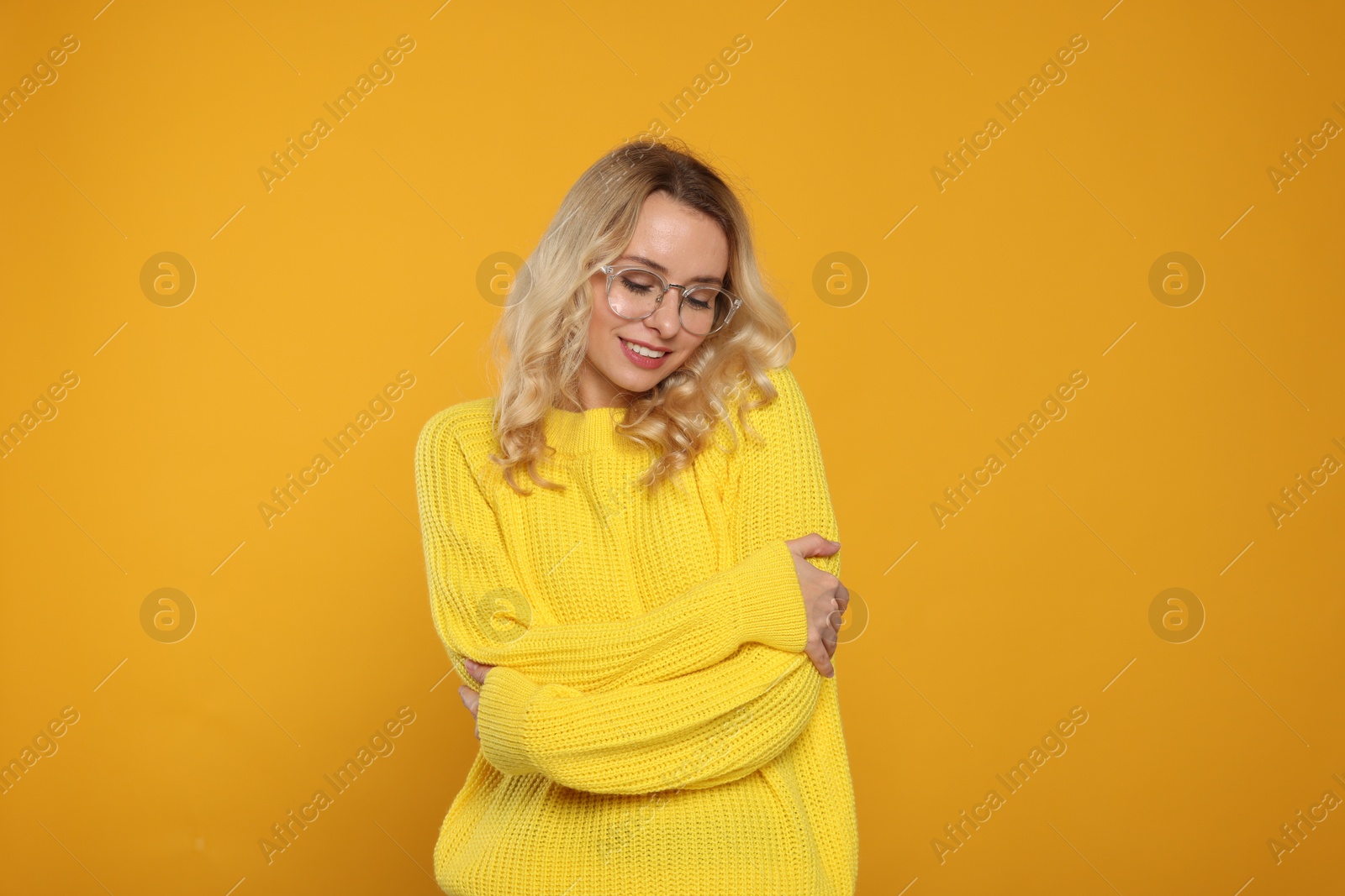 Photo of Happy woman in stylish warm sweater and eyeglasses on orange background