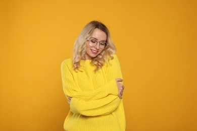 Happy woman in stylish warm sweater and eyeglasses on orange background