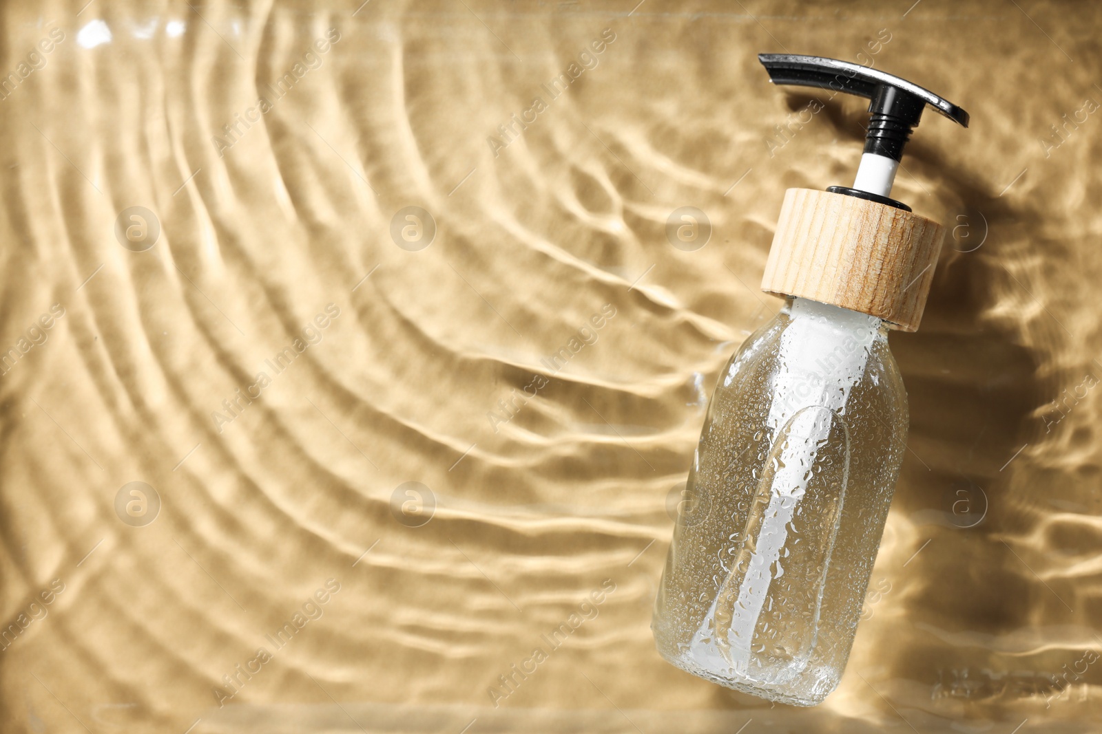 Photo of Bottle of cosmetic product in water on beige background, top view. Space for text