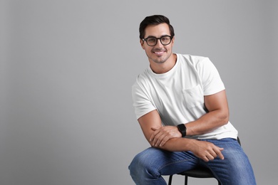 Photo of Handsome young man sitting on stool against grey background. Space for text