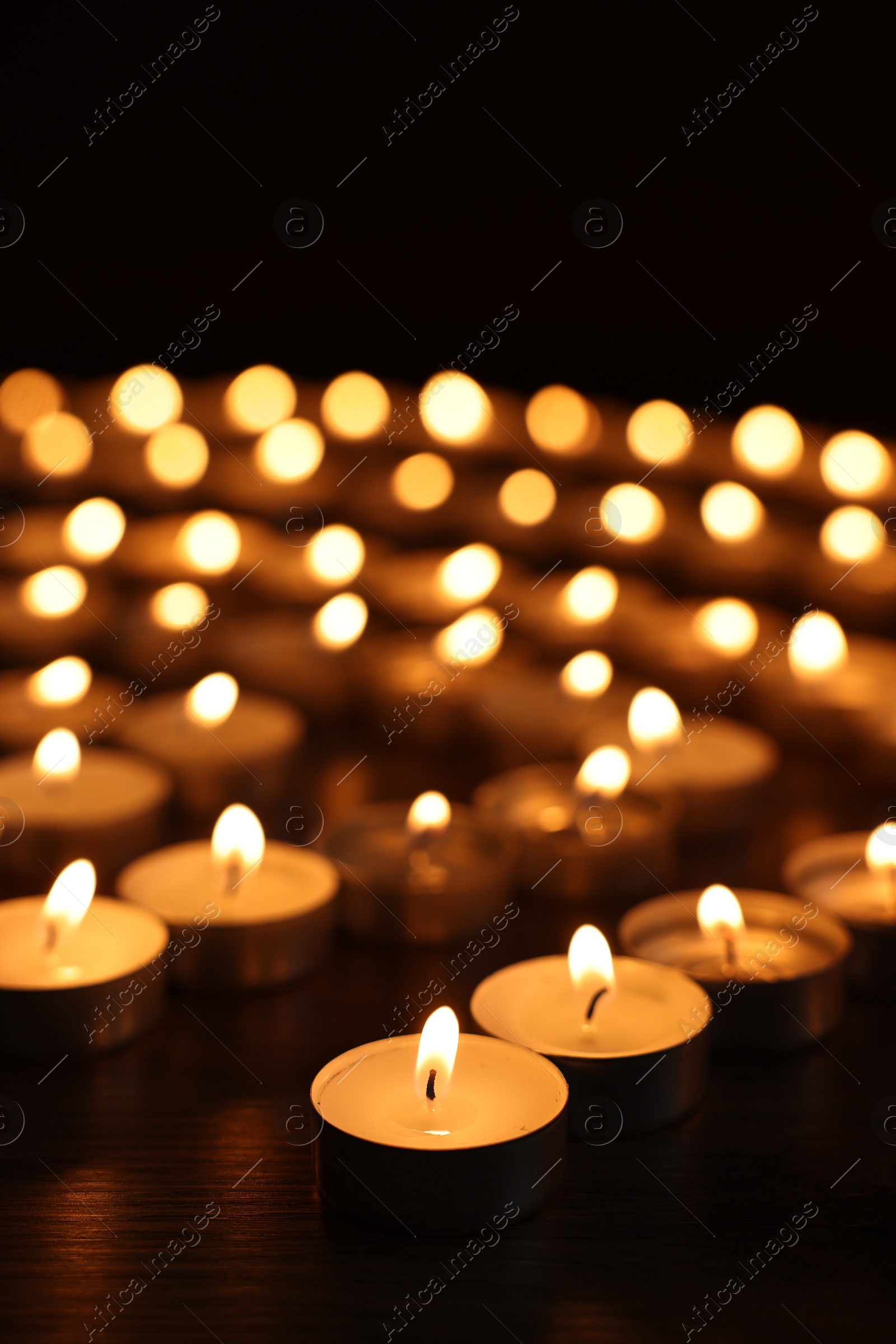 Photo of Burning candles on wooden table in darkness