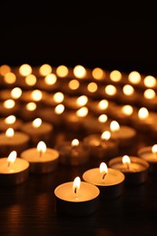 Burning candles on wooden table in darkness