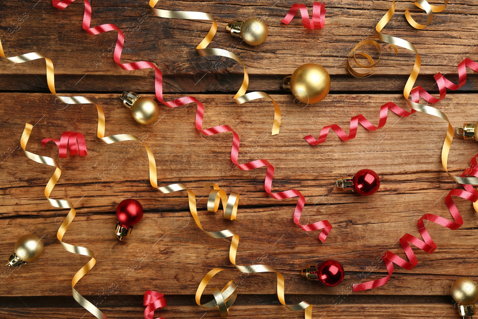 Photo of Shiny serpentine streamers and Christmas balls on wooden background, flat lay