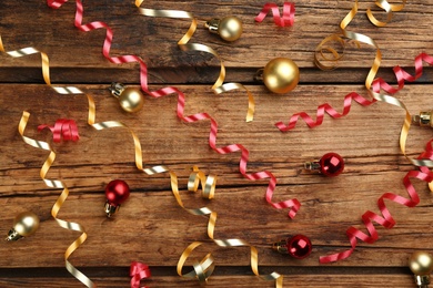 Shiny serpentine streamers and Christmas balls on wooden background, flat lay