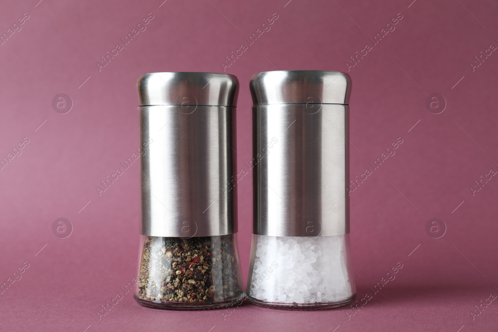 Photo of Salt and pepper shakers on dark pink background, closeup