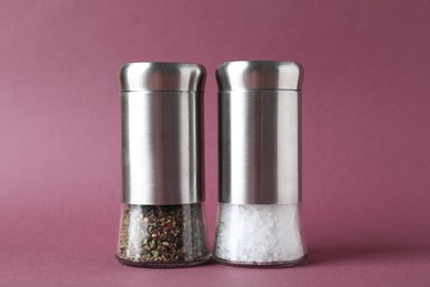 Photo of Salt and pepper shakers on dark pink background, closeup