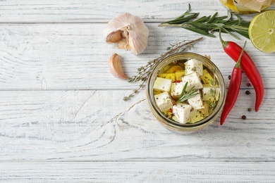 Flat lay composition with pickled feta cheese in jar on white wooden table, space for text