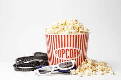 Bucket of fresh popcorn, film footage and 3D glasses on white background. Cinema snack