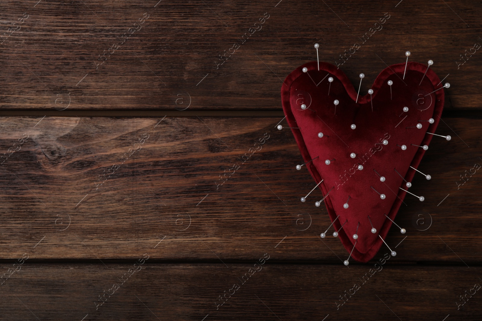 Photo of Top view of heart shaped cushion with sewing pins on wooden background, space for text. Relationship problems concept