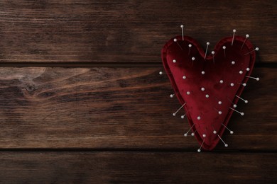 Photo of Top view of heart shaped cushion with sewing pins on wooden background, space for text. Relationship problems concept