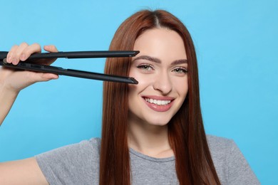 Photo of Beautiful woman with hair iron on light blue background