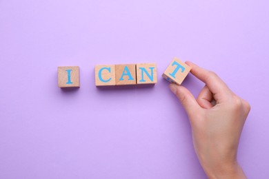 Photo of Motivation concept. Woman changing phrase from I Can't into I Can by removing wooden cube with letter T on violet background, top view