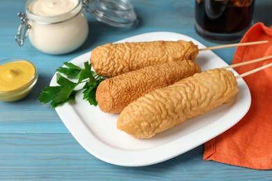 Photo of Delicious deep fried corn dogs with parsley and sauces on turquoise wooden table, closeup