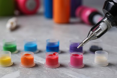 Photo of Dipping tattoo machine needle into ink on light grey table, closeup