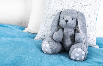Photo of Cute toy rabbit sitting on bed indoors. Space for text