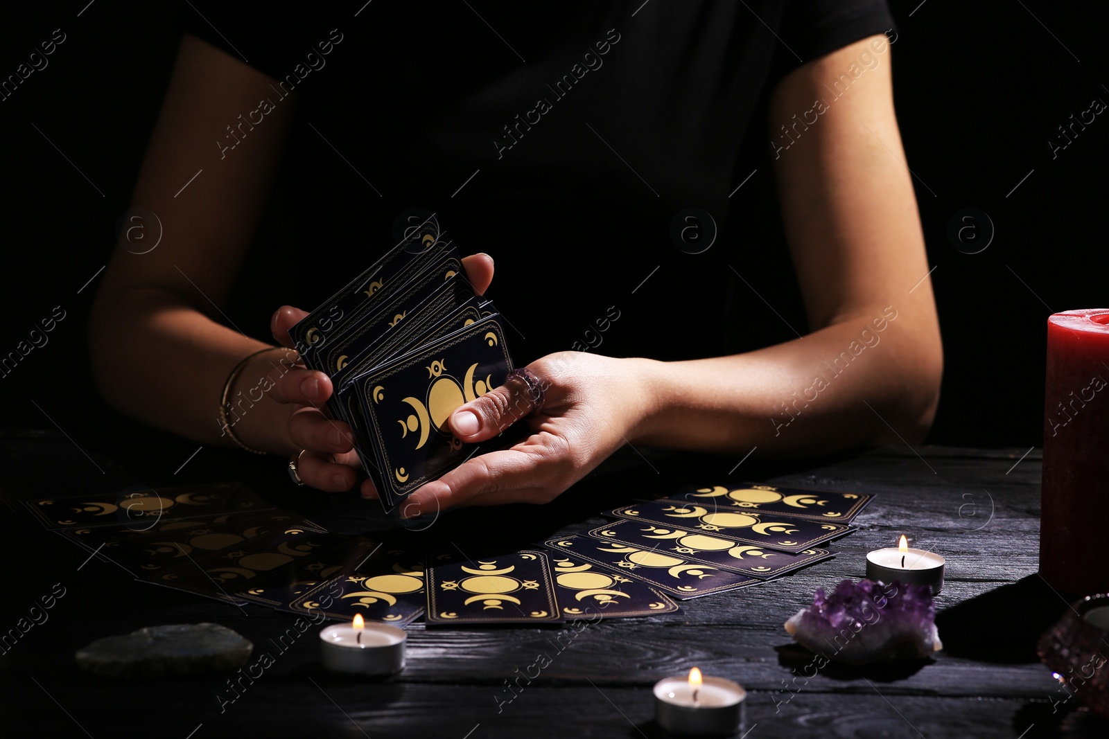 Photo of Soothsayer shuffling tarot cards at table in darkness. Fortune telling