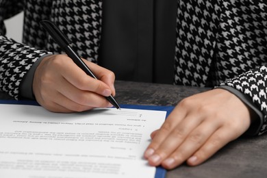 Photo of Woman signing document at dark table, closeup