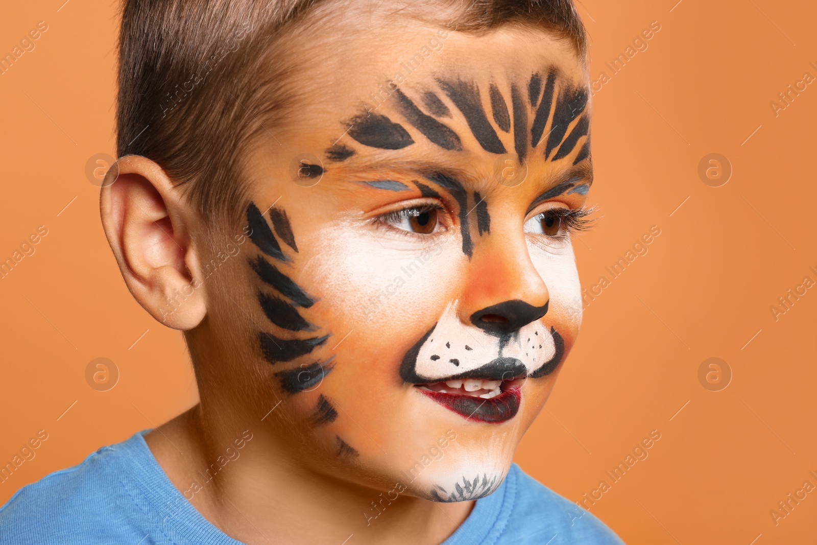 Photo of Cute little boy with face painting on orange background