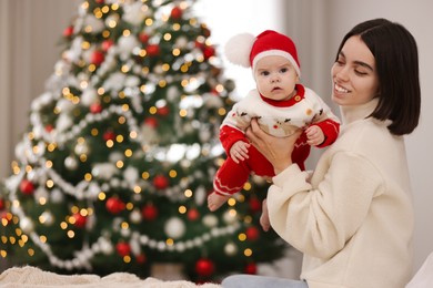 Photo of Happy young mother with her cute baby against blurred festive lights, space for text. Winter holiday