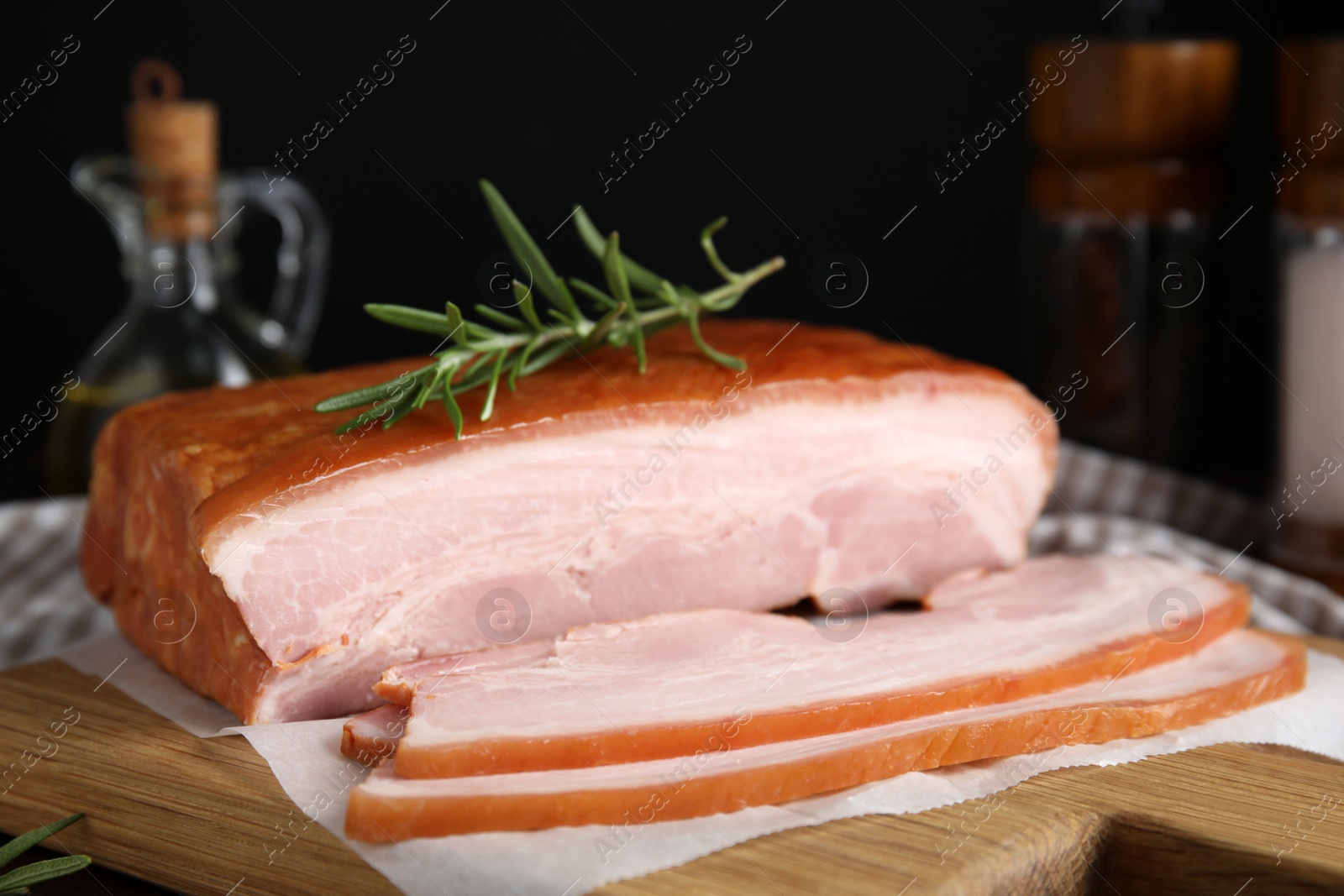 Photo of Delicious smoked bacon with rosemary on wooden board, closeup