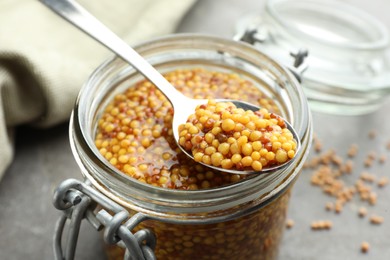 Photo of Whole grain mustard in jar and spoon on table, closeup