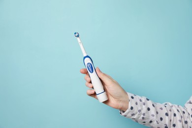 Woman holding electric toothbrush on light blue background, closeup