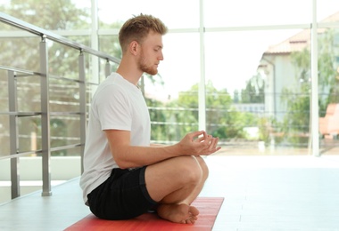 Photo of Handsome young man practicing zen yoga indoors