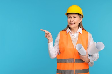 Photo of Architect in hard hat with drafts pointing at something on light blue background, space for text