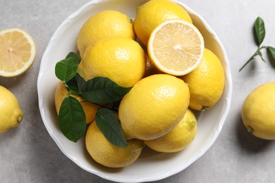 Fresh lemons and green leaves on grey table, top view