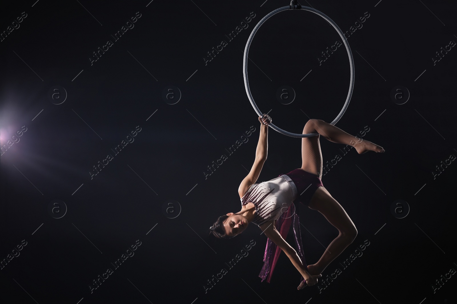 Photo of Young woman performing acrobatic element on aerial ring against dark background. Space for text