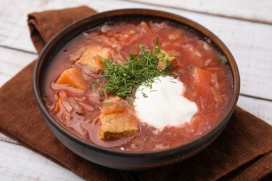 Photo of Tasty borscht with sour cream in bowl on white wooden table, closeup