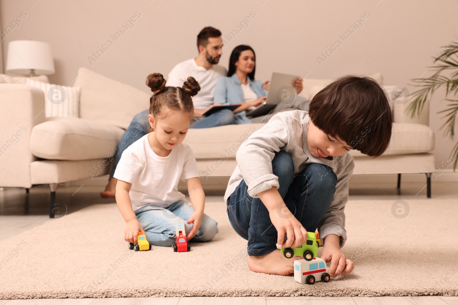 Photo of Cute children playing with toys while parents using gadgets on sofa in living room