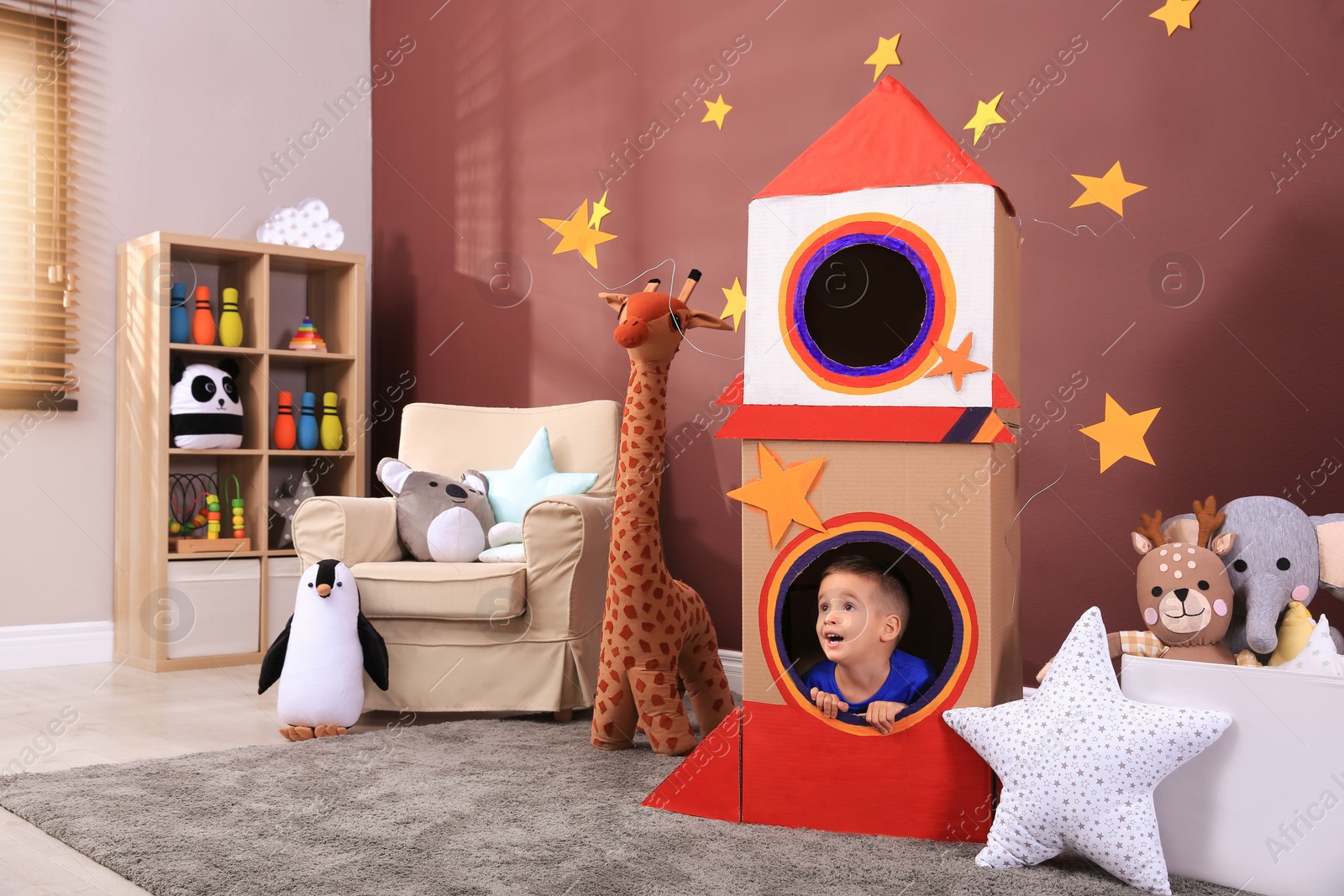 Photo of Cute little boy playing on floor near cardboard rocket  at home. Child's room interior