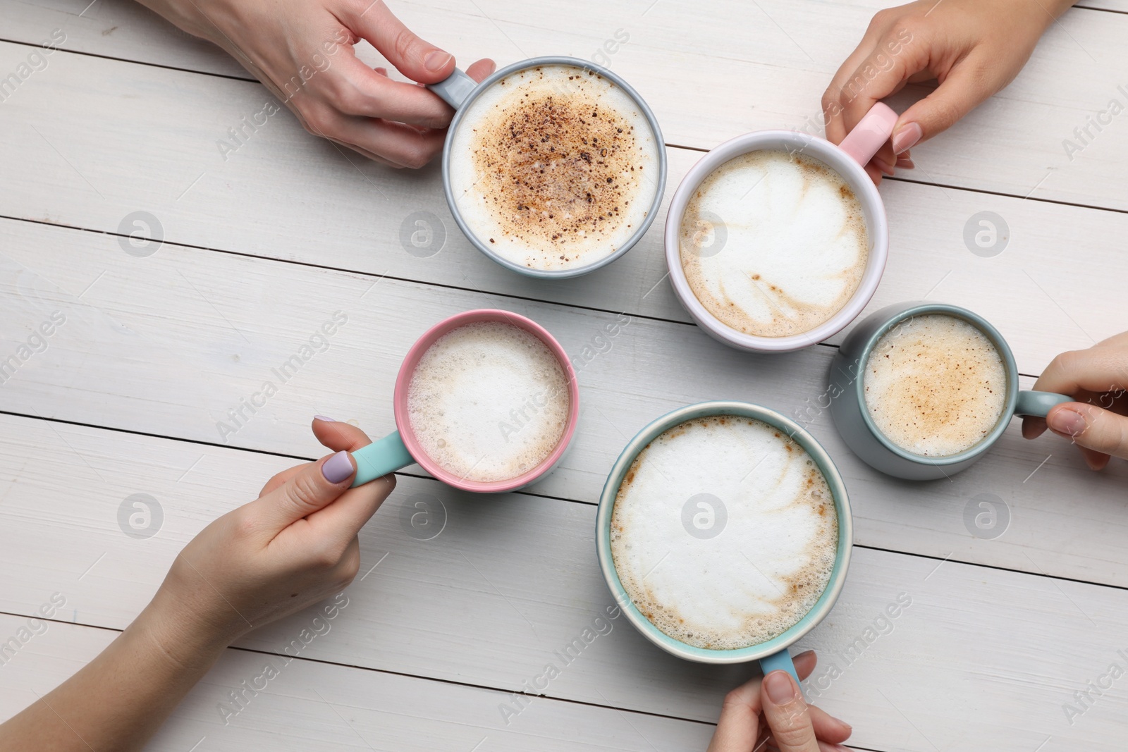 Photo of People holding different cups with aromatic hot coffee at white wooden table, top view