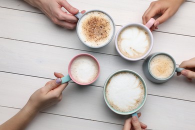 Photo of People holding different cups with aromatic hot coffee at white wooden table, top view