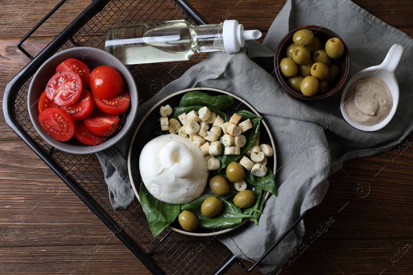 Photo of Delicious burrata cheese served with olives, croutons, basil and tomatoes on wooden table, top view