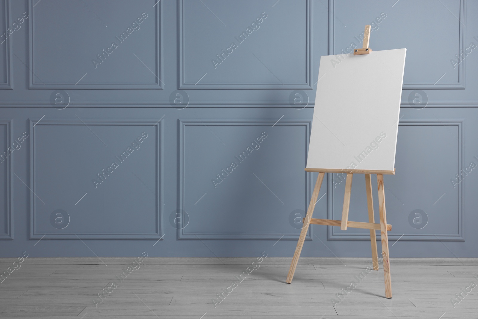 Photo of Wooden easel with blank canvas near grey wall indoors. Space for text