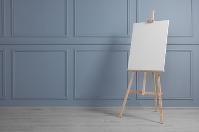 Wooden easel with blank canvas near grey wall indoors. Space for text