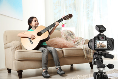 Image of Little music teacher recording guitar lesson indoors